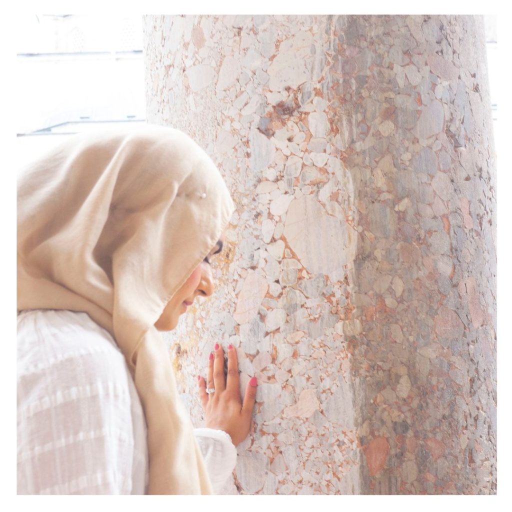 A neutral coloured Image of Heena with her head bowed down and eyes closed, wearing a hijab with her hand touching a marble pillar on her trip to Istanbul, Turkey.